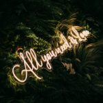 all you need is love wedding neon sign with greenery backdrop