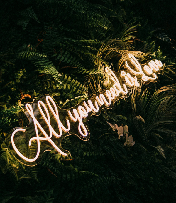 all you need is love wedding neon sign with greenery backdrop