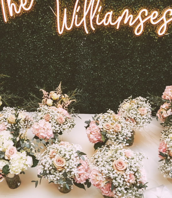 the williamses wedding neon sign with last name on greenery backdrop, flowers on table