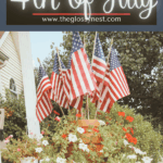A stack of terra cotta pots filled with flowers displays several small American flags. Text above reads, "Primitive Decor Ideas for 4th of July www.theglossynest.com.