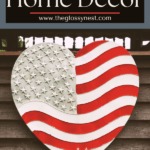 A large heart-shaped decoration painted like the American flag is displayed outdoors in front of a wooden fence. Text above reads “Farmhouse Patriotic Home Decor” and “www.theglossynest.com.”.